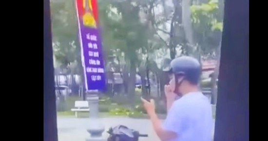 Nam thanh niên đi xe máy thả hai tay vừa xem điện thoại, vừa xỉa răng